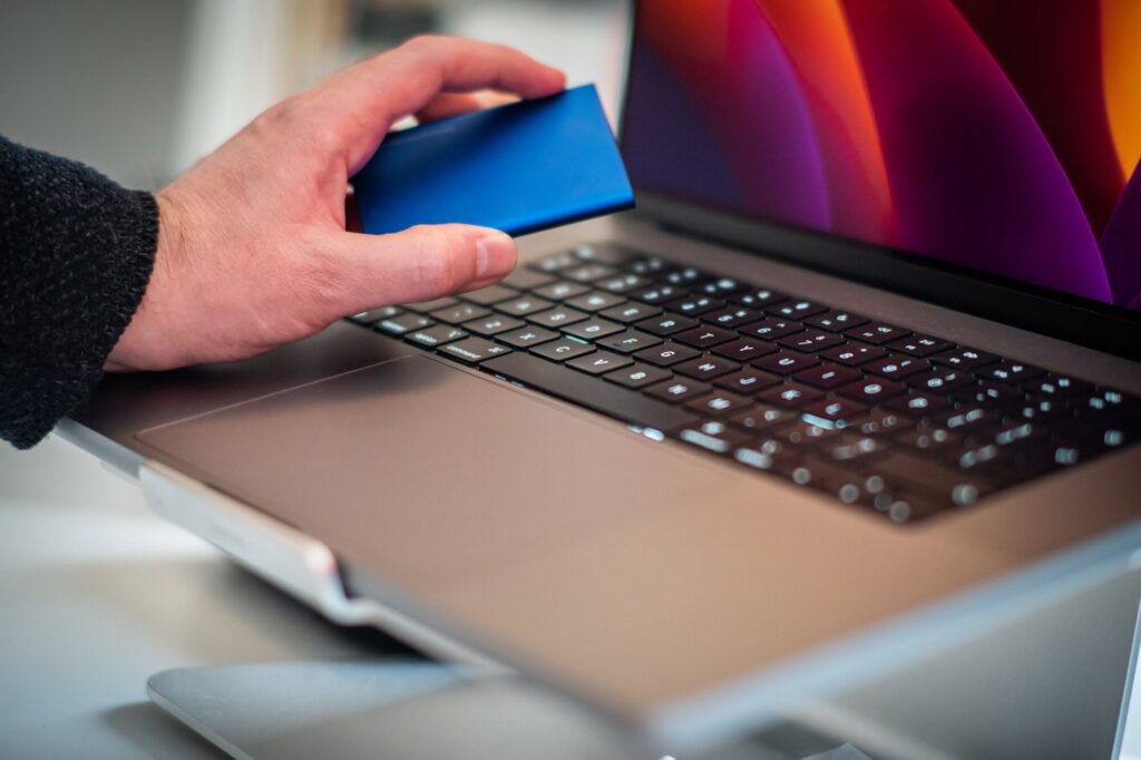 Disque SSD externe compact tenu à la main au-dessus d'un ordinateur portable moderne